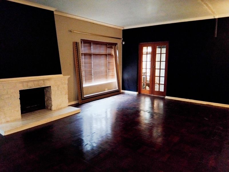 Spacious living room featuring a stone fireplace, dark parquet flooring, and classic French doors, offering a versatile layout with natural light.