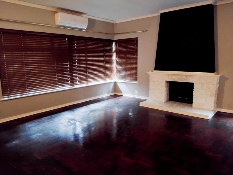 Spacious living room featuring polished timber flooring, a prominent stone fireplace, and a wall-mounted air conditioning unit.