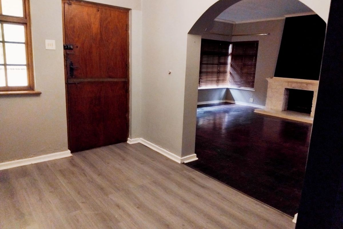 An empty living area featuring an arched transition to a secondary space with a fireplace, laminate flooring, and a classic timber stable door.