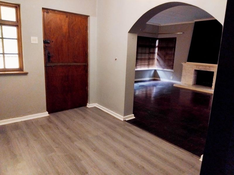 An empty living area featuring an arched transition to a secondary space with a fireplace, laminate flooring, and a classic timber stable door.