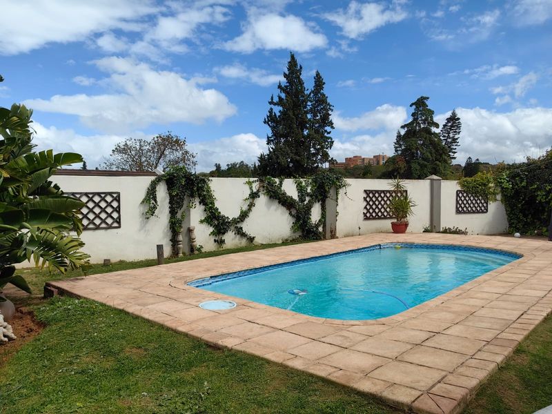 Outdoor swimming pool area featuring a paved surround and a high boundary wall with decorative trellis panels.