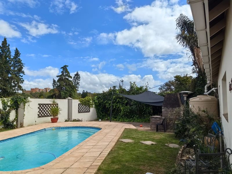 Outdoor pool area featuring a paved surround, built-in brick braai, and a water storage tank, set within a private garden with perimeter walling.
