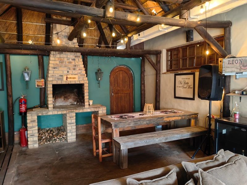 A rustic covered patio area featuring a traditional thatched roof, exposed timber beams, and a built-in brick fireplace, ideal for outdoor entertaining.