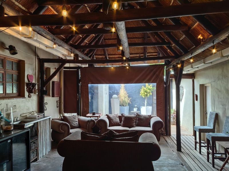A rustic covered patio featuring a traditional thatched roof, exposed timber beams, built-in bar area, and timber decking, perfect for outdoor entertaining.