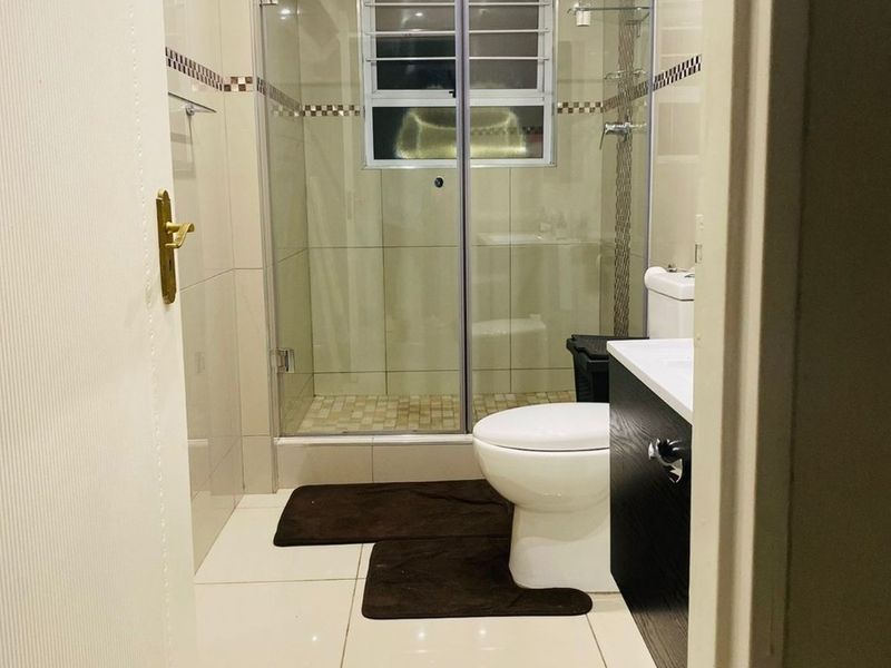 A modern, well-maintained bathroom featuring a glass-enclosed shower, built-in vanity, and neutral tiled finishes throughout.