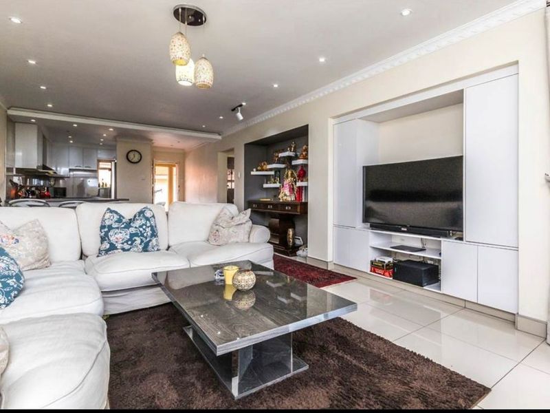 Spacious open-plan living area featuring polished tiled floors, recessed lighting, and a custom built-in media wall with integrated shelving.