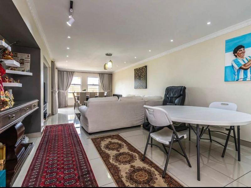 Spacious open-plan living and dining area featuring polished porcelain floor tiles, recessed downlighting, and a built-in shelving unit.