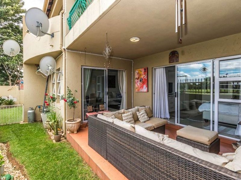A covered ground-floor patio featuring tiled flooring and sliding glass door access to the interior, overlooking a small private garden area.