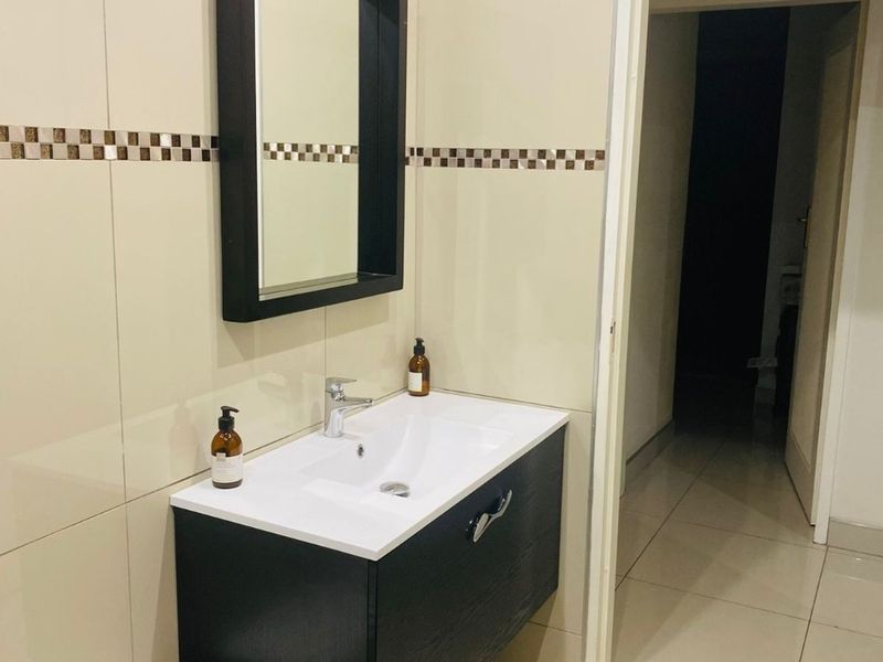A modern bathroom featuring a wall-mounted vanity with a ceramic basin, chrome mixer tap, and a matching wall mirror against tiled walls.