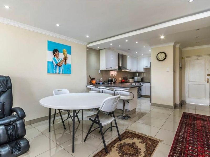 An open-plan living and kitchen area featuring tiled flooring, recessed lighting, and a functional kitchen with built-in cabinetry and a breakfast counter.