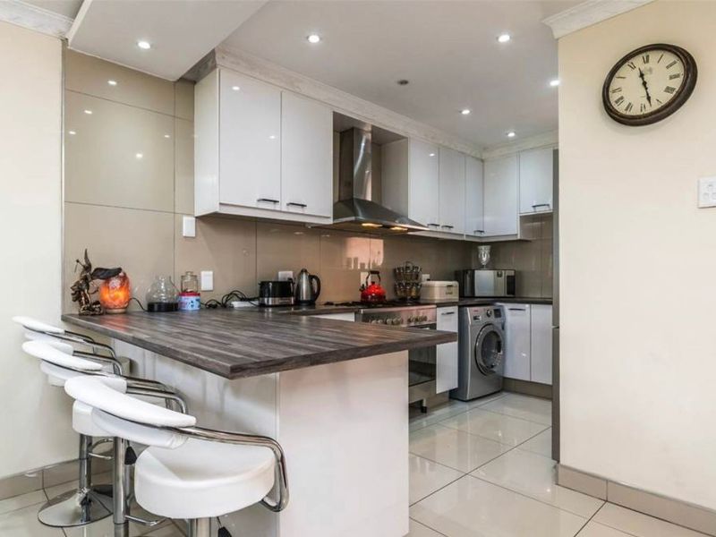 Modern kitchen featuring white cabinetry, a breakfast bar with a dark wood-look countertop, stainless steel appliances, and tiled flooring.