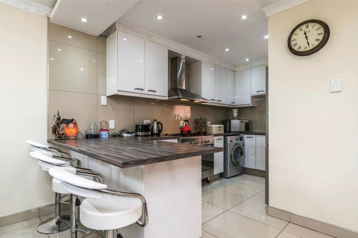 Modern kitchen featuring white cabinetry, a breakfast bar with a dark wood-look countertop, stainless steel appliances, and tiled flooring.