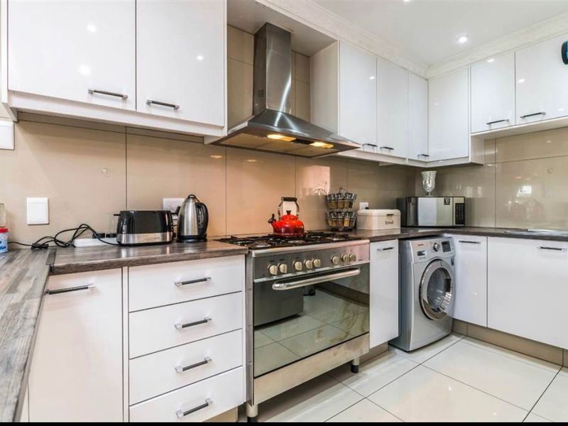 Modern kitchen featuring white high-gloss cabinetry, stainless steel appliances, gas hob, extractor fan, and tiled splashbacks with integrated laundry space.