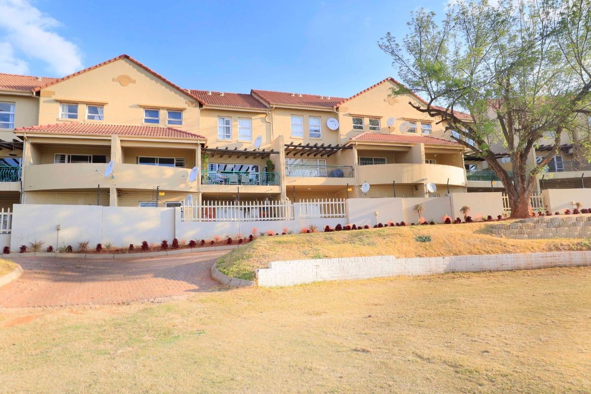 Rear view of a multi-unit apartment complex featuring private balconies, timber pergolas, and a landscaped communal garden area with paved access.