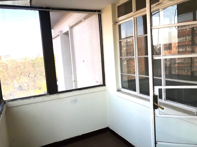 An enclosed balcony or sunroom featuring metal-framed windows and doors, offering a bright space with potential for renovation or modern styling.