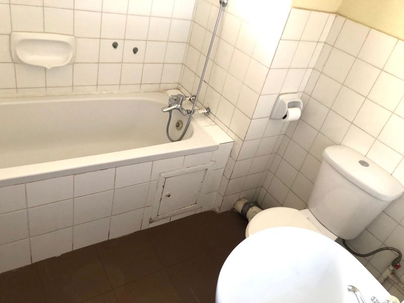 A dated bathroom featuring a standard bathtub, toilet, and tiled finishes, requiring modernization to improve its overall condition and aesthetic appeal.