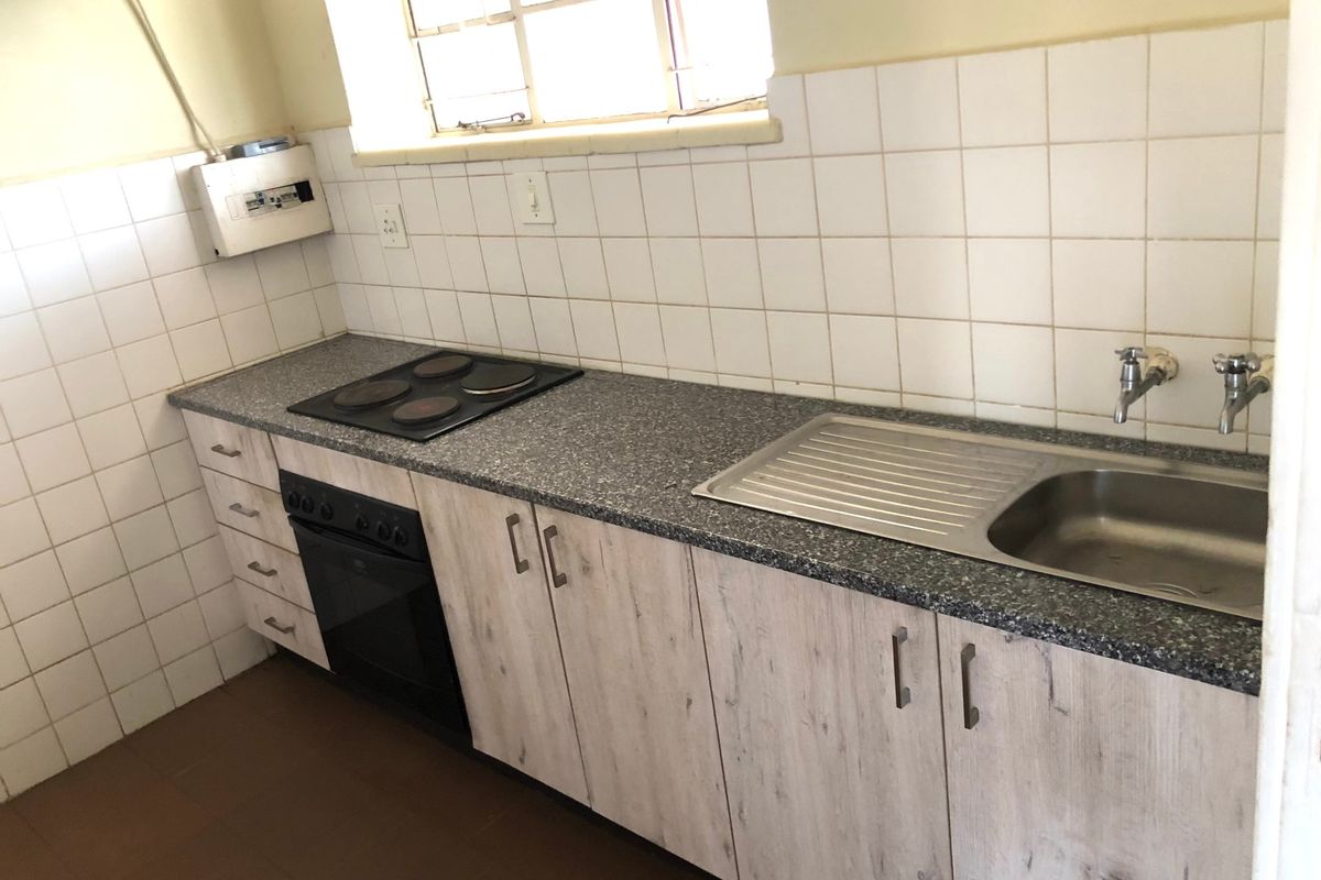 A functional kitchen featuring wood-look cabinetry, a granite-effect laminate countertop, built-in oven and hob, and a stainless steel sink with tiled splashback.