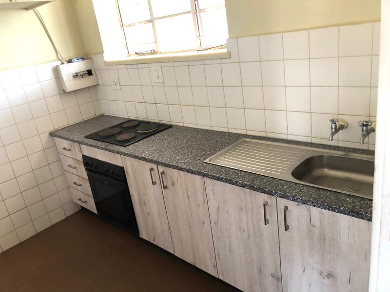 A functional kitchen featuring wood-look cabinetry, a granite-effect laminate countertop, built-in oven and hob, and a stainless steel sink with tiled splashback.