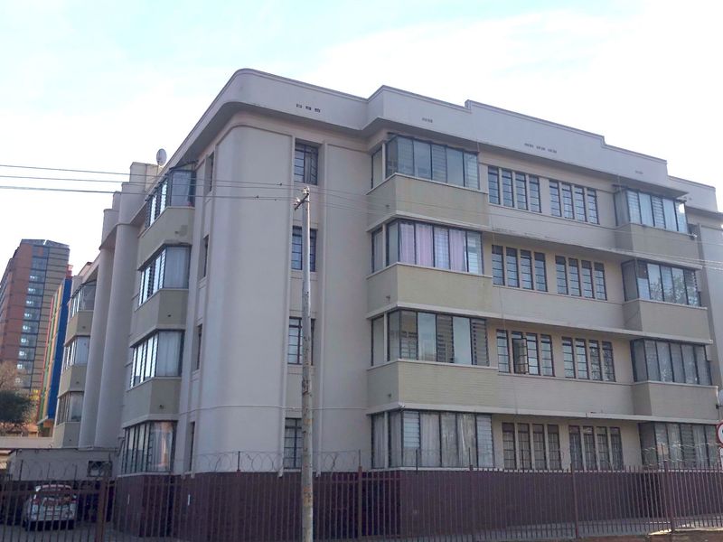 Exterior view of a multi-story apartment building featuring a classic facade with steel-framed windows and secure perimeter fencing.