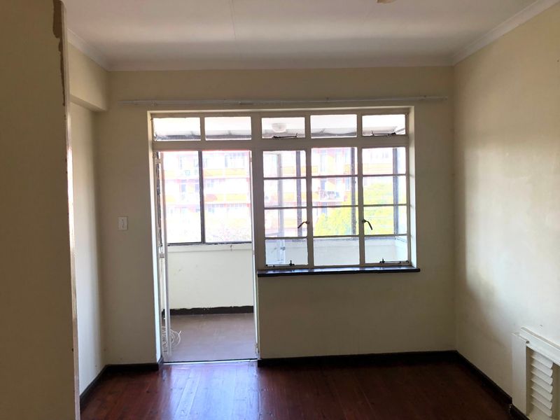 An empty living room featuring timber flooring and direct access to an enclosed balcony through a multi-pane door and window assembly.