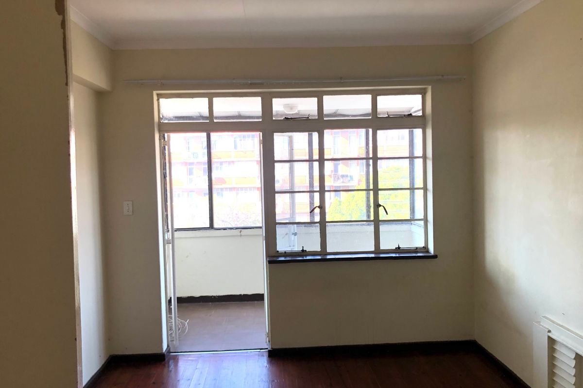 An empty living room featuring timber flooring and direct access to an enclosed balcony through a multi-pane door and window assembly.