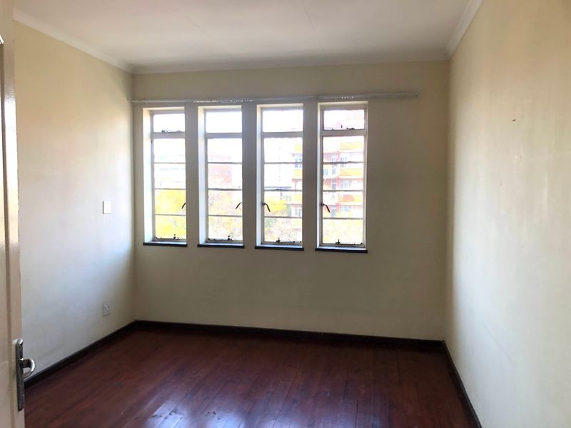 An empty bedroom featuring original timber flooring and large steel-framed windows, providing a blank canvas for potential interior design updates.