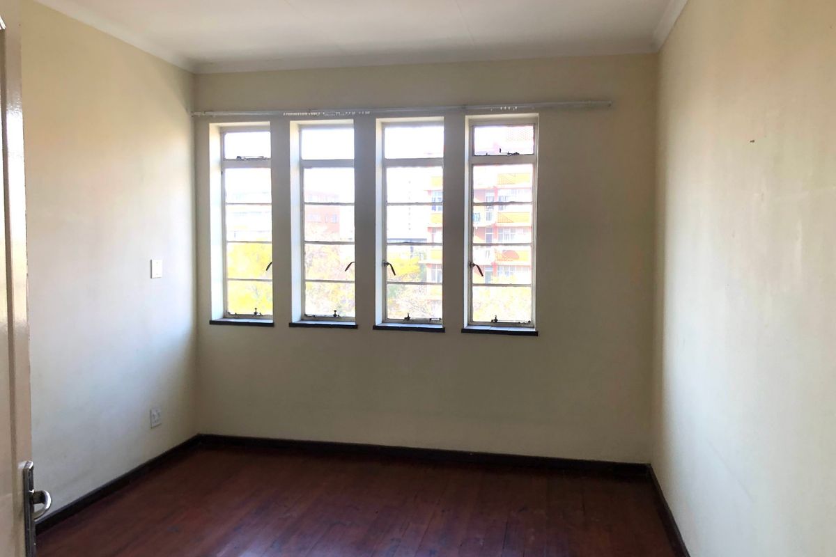 An empty bedroom featuring original timber flooring and large steel-framed windows, providing a blank canvas for potential interior design updates.