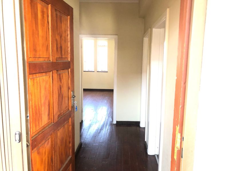 A vacant hallway featuring dark timber flooring and wooden door frames, leading into an adjacent room with natural light.