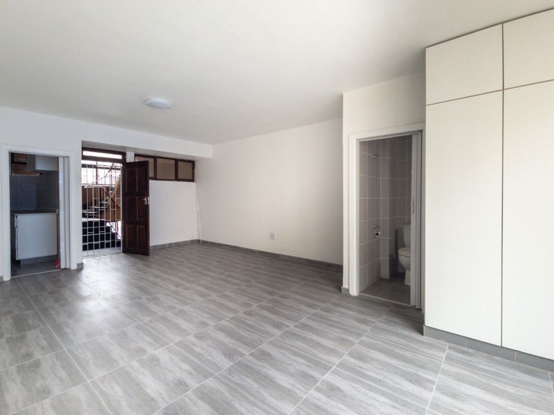 A bright, empty living area featuring modern grey tiled flooring, built-in storage cabinetry, and direct access to an adjoining bathroom and secondary space.