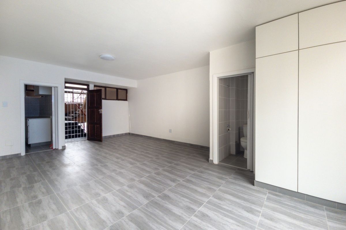 A bright, empty living area featuring modern grey tiled flooring, built-in storage cabinetry, and direct access to an adjoining bathroom and secondary space.