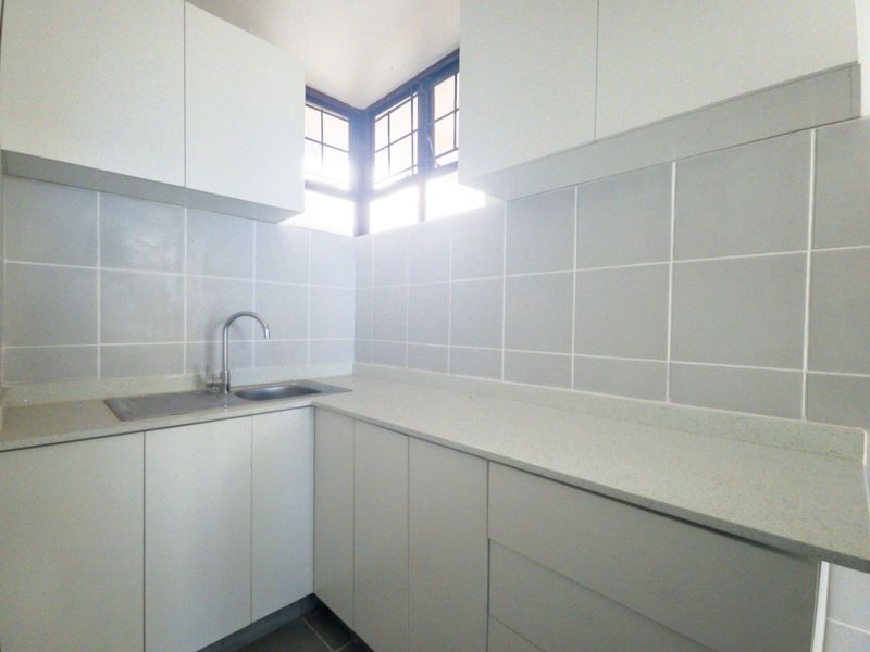 A clean and functional scullery featuring white built-in cabinetry, stone countertops, a stainless steel sink, and a tiled backsplash.