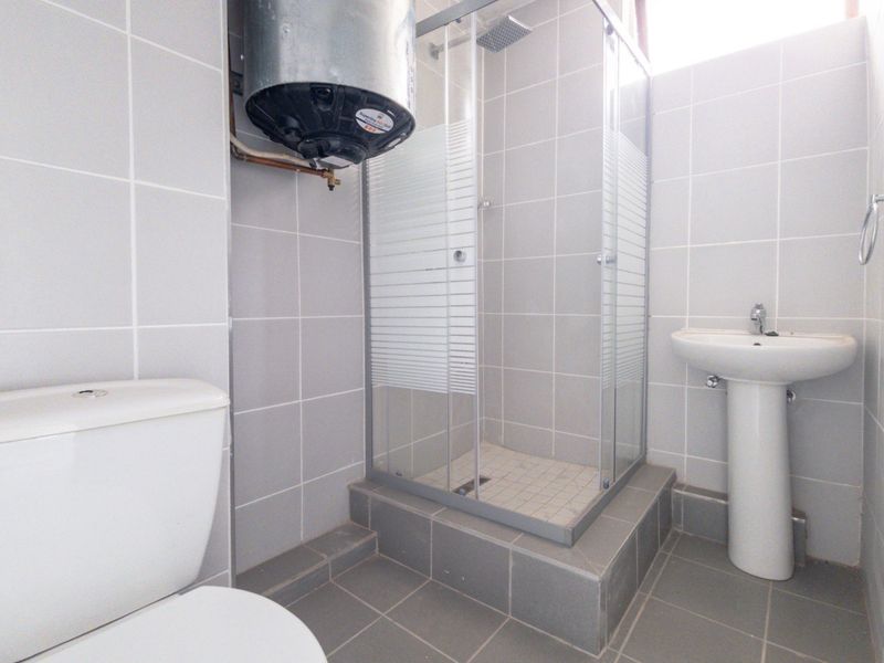 A functional bathroom featuring a tiled shower enclosure, pedestal basin, toilet, and an exposed electric water heater unit.