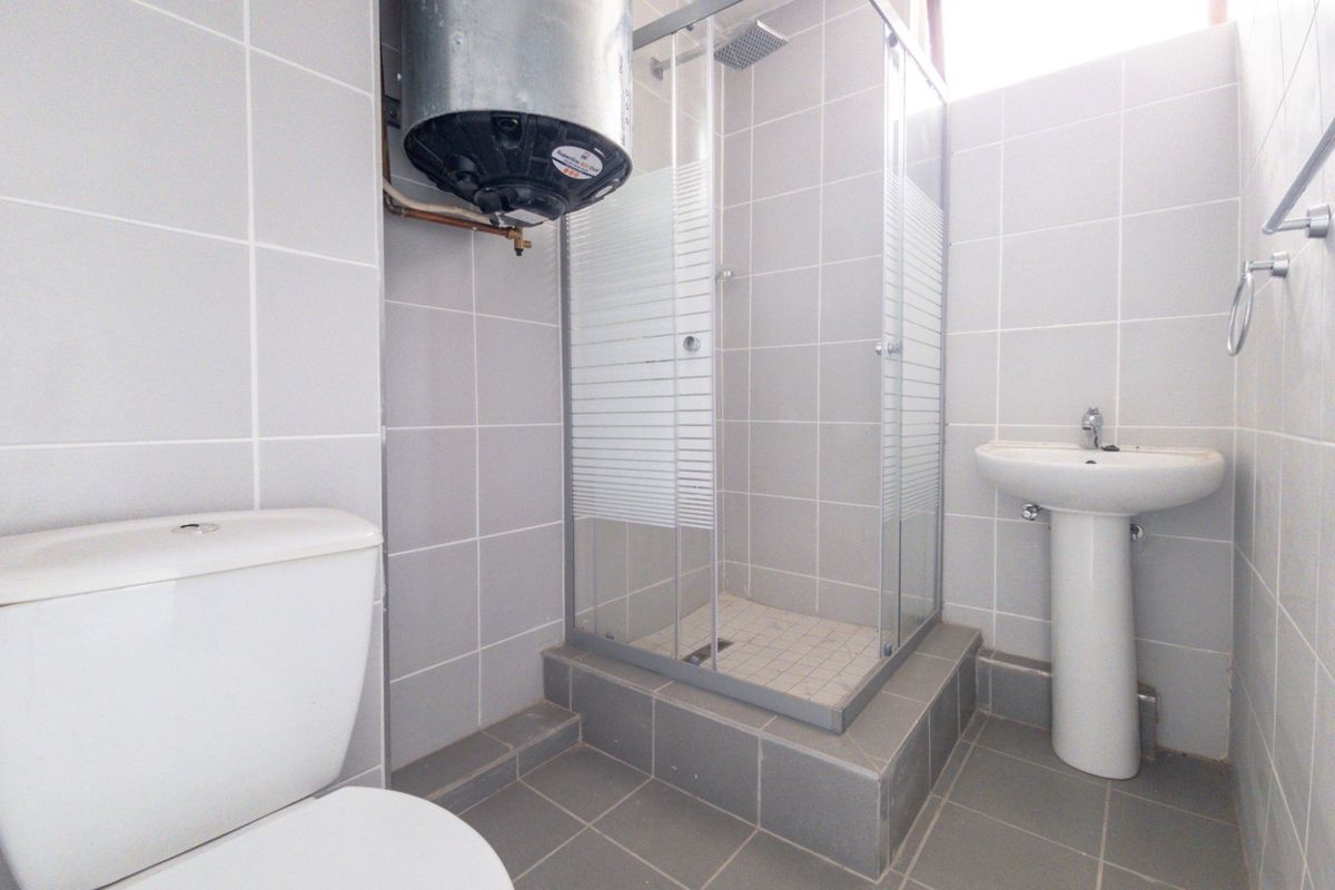 A functional bathroom featuring a tiled shower enclosure, pedestal basin, toilet, and an exposed electric water heater unit.