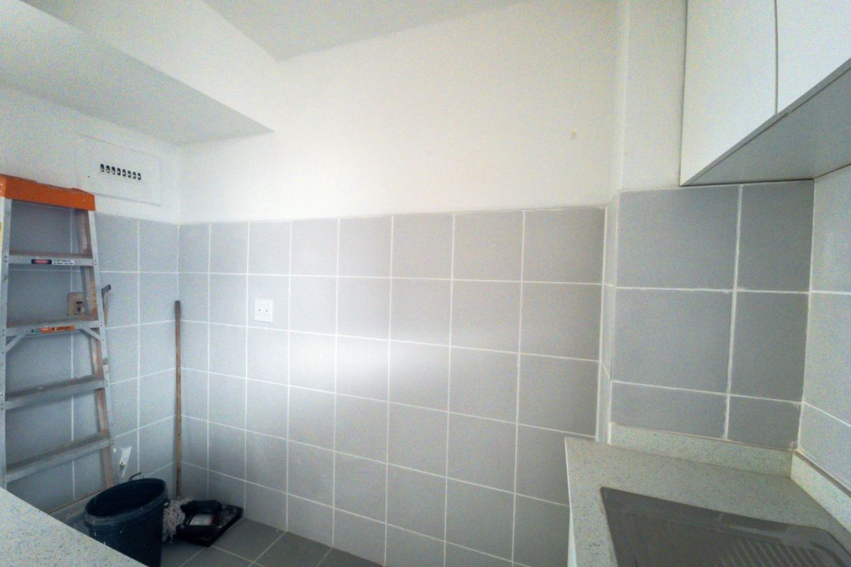 A functional kitchen area featuring neutral wall tiles, built-in cabinetry, and a clean countertop surface, ready for personalization.