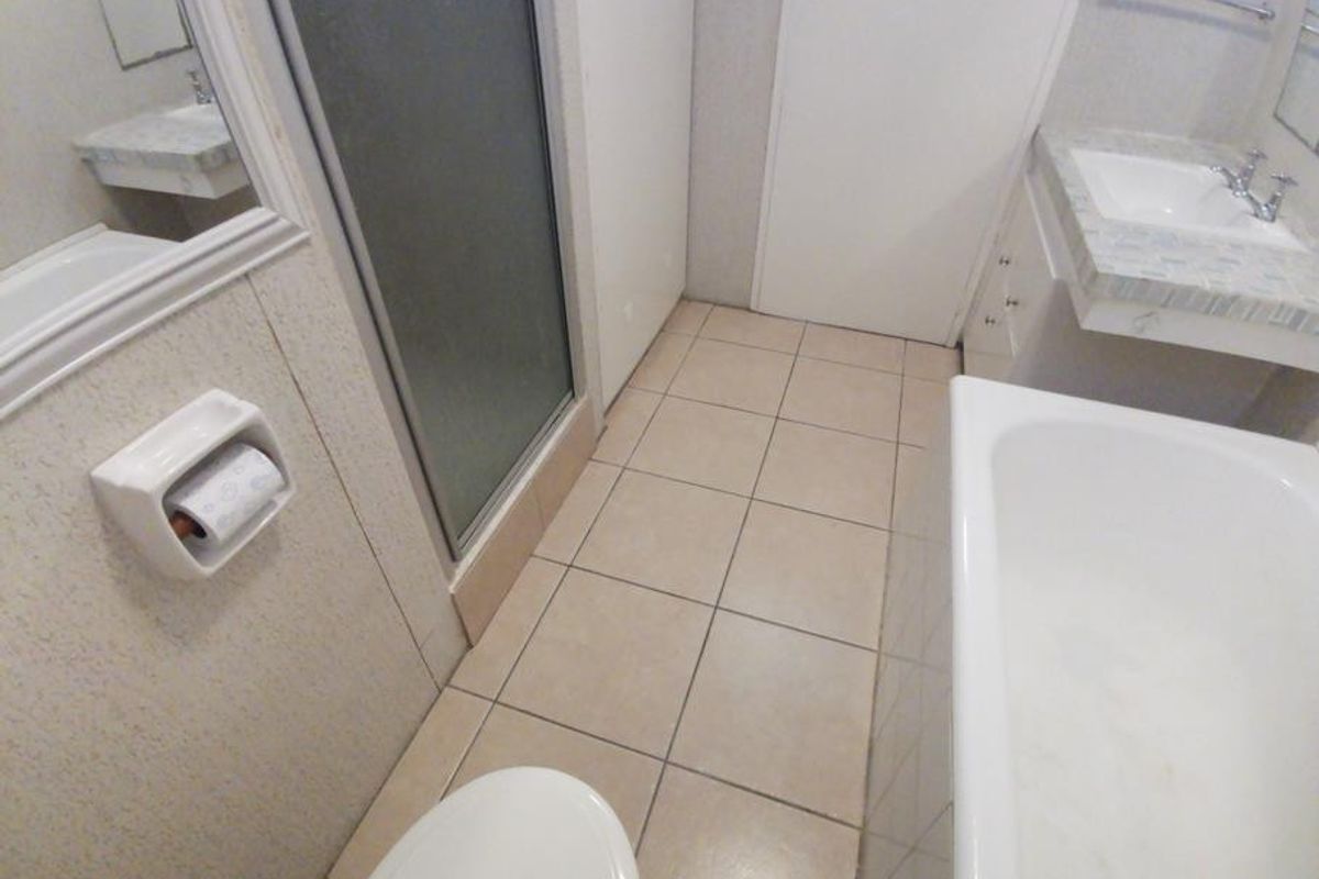 A functional bathroom featuring a bathtub, separate shower enclosure, and a built-in vanity with a basin, requiring cosmetic updates to modernize the space.