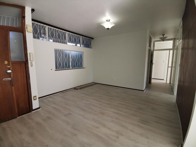 An empty living room featuring light-toned laminate flooring, security gates on windows, and an intercom system, offering a clean canvas for personalization.