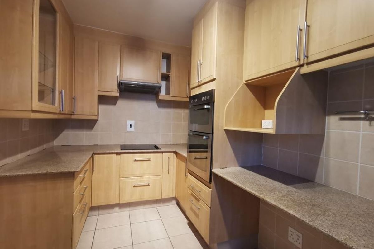 A functional kitchen featuring light wood cabinetry, granite countertops, a double wall oven, and an electric cooktop with a tiled backsplash.