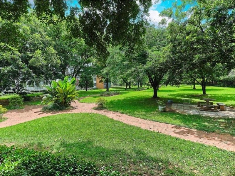 A lush, well-maintained communal garden featuring mature trees, expansive green lawns, and paved pathways providing a tranquil outdoor space.