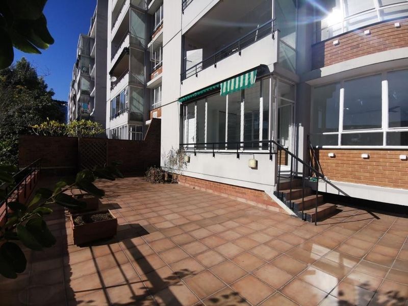 A spacious ground-floor tiled patio area featuring a brick boundary wall, metal railings, and a retractable awning, providing direct access to the apartment.
