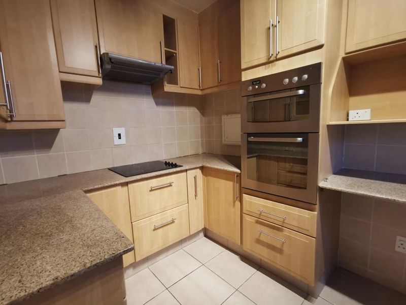 A functional kitchen featuring light wood cabinetry, granite countertops, a built-in double oven, and an electric hob with an extractor fan.