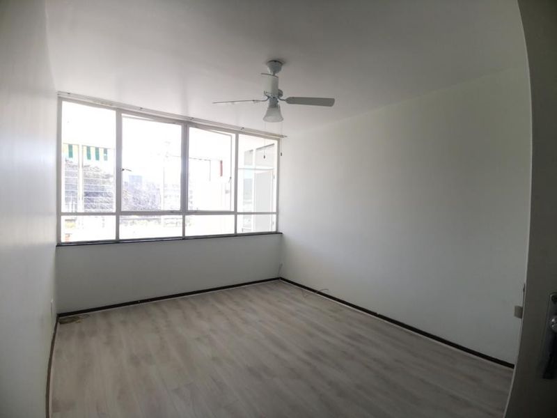 A bright, empty bedroom featuring light-toned laminate flooring, a ceiling fan, and large windows that provide ample natural light.