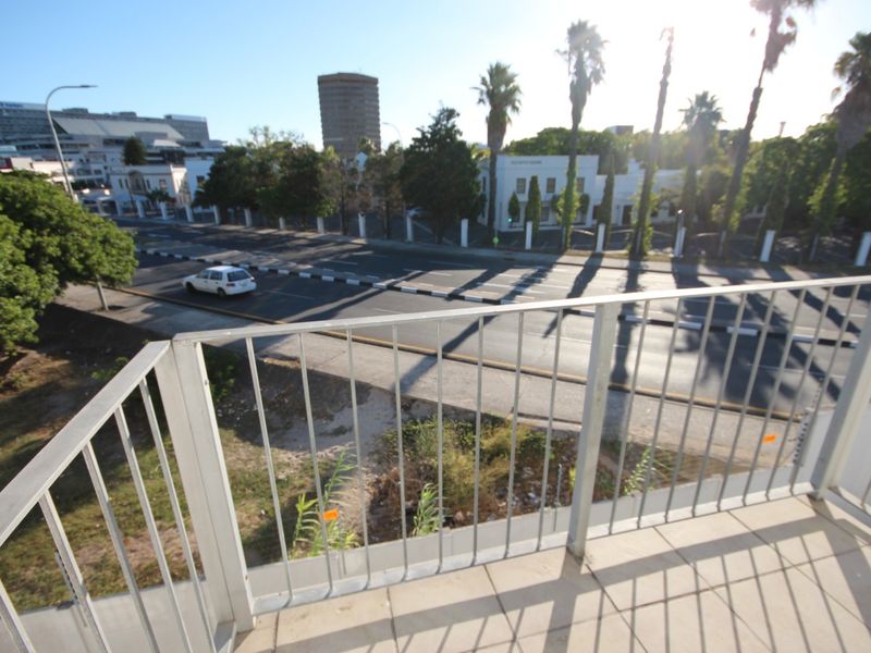 A balcony featuring a metal balustrade and tiled flooring, offering an elevated view of the surrounding street and urban landscape.