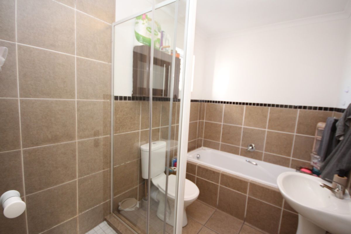 A functional bathroom featuring a shower enclosure, bathtub, pedestal basin, and toilet with neutral brown wall and floor tiling.