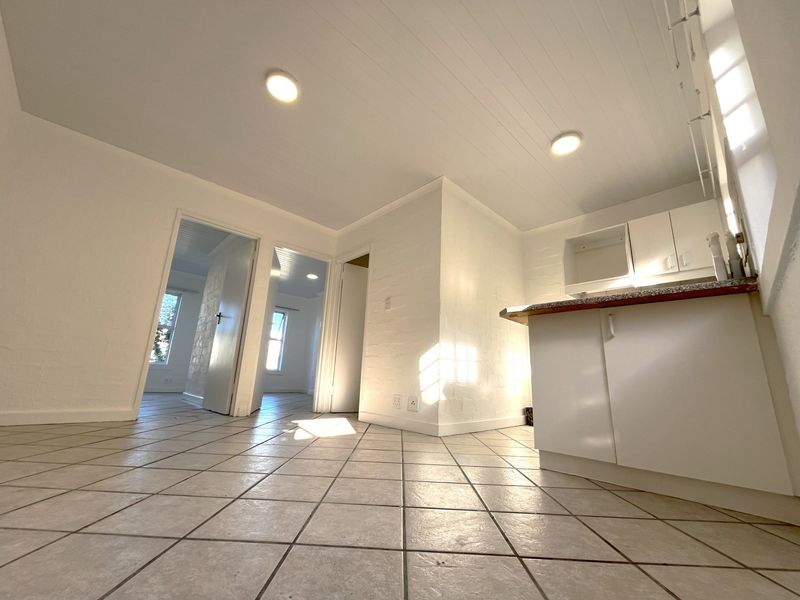 An open-plan living and kitchen area featuring tiled flooring, white cabinetry with granite countertops, and a clean, neutral aesthetic throughout.