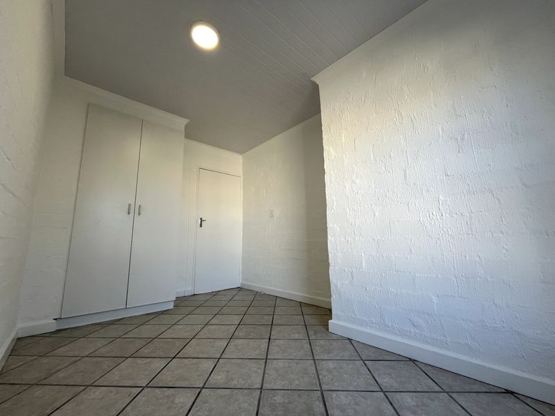 A clean, empty hallway featuring neutral tiled flooring, built-in storage cupboards, and a textured white wall finish.