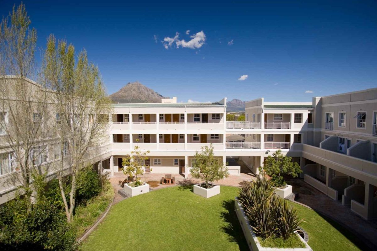 A well-maintained apartment complex courtyard featuring a central lawn, landscaped garden beds, and multi-level balconies with mountain views.