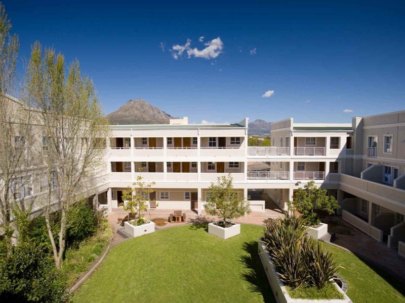 A well-maintained apartment complex courtyard featuring a central lawn, landscaped garden beds, and multi-level balconies with mountain views.