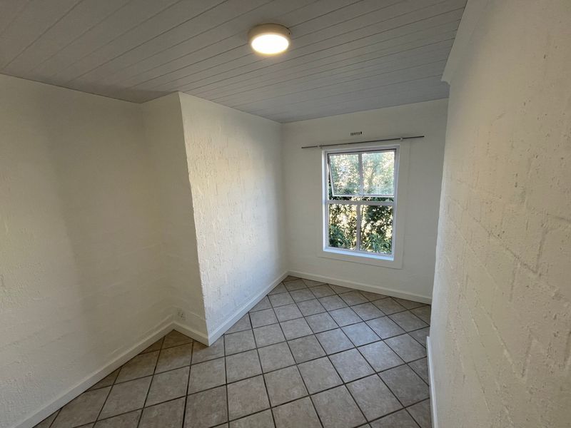 A bright, empty bedroom featuring textured white brick walls, tiled flooring, and a tongue and groove ceiling with a central light fixture.