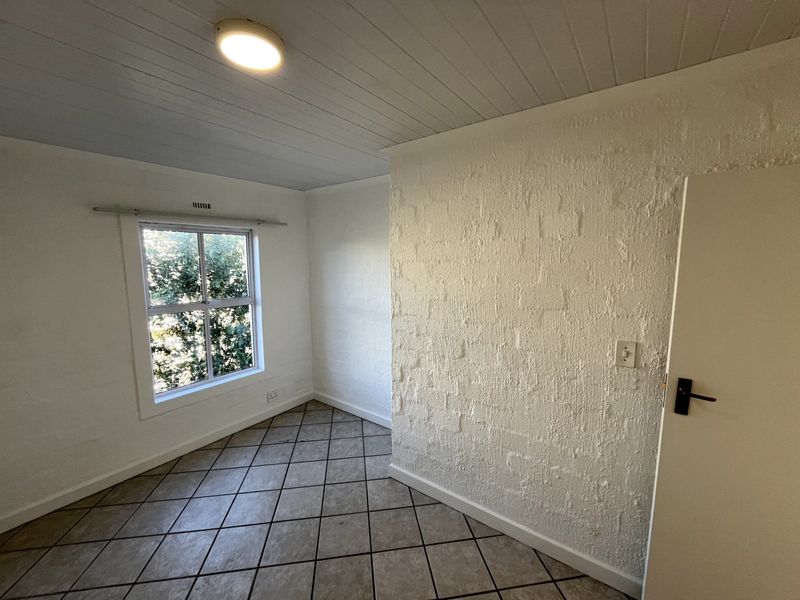 An empty bedroom featuring tiled flooring, a textured feature wall, and a timber panel ceiling with a central light fixture.