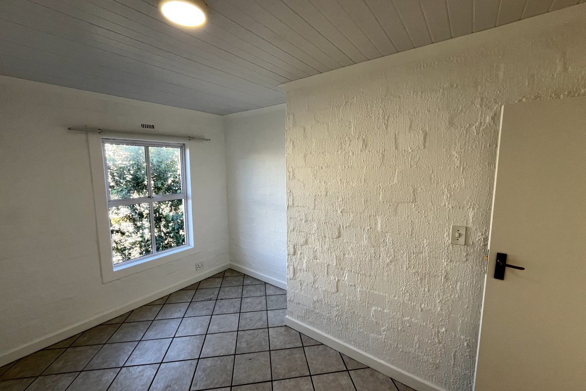An empty bedroom featuring tiled flooring, a textured feature wall, and a timber panel ceiling with a central light fixture.